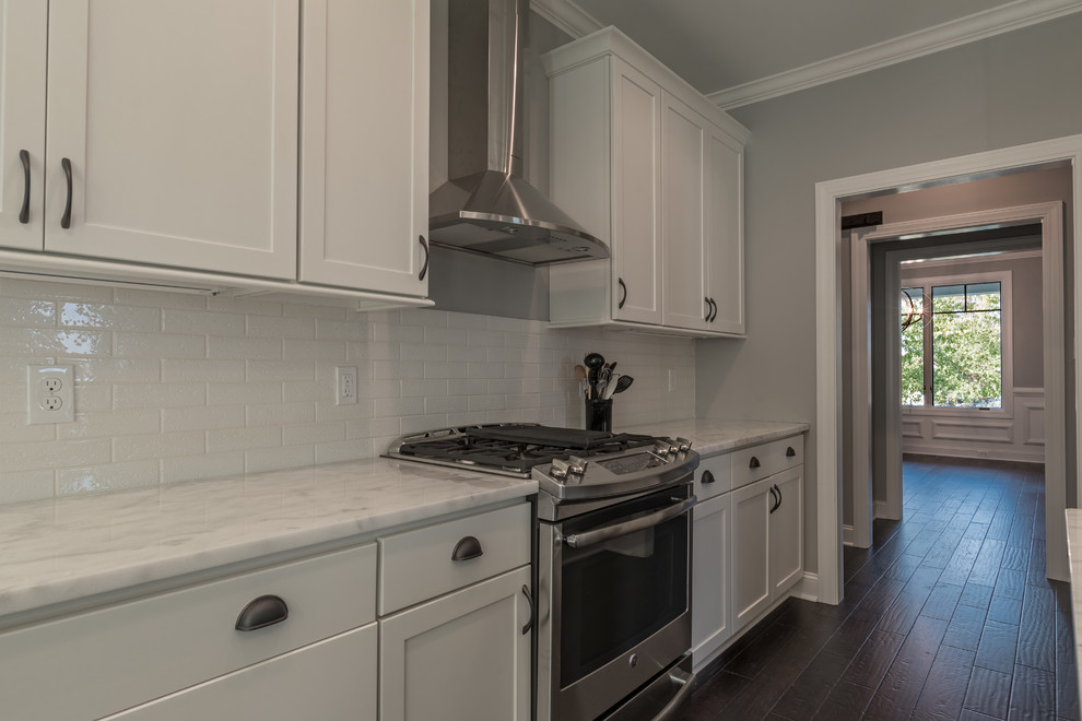 Eat-in kitchen - mid-sized transitional dark wood floor eat-in kitchen idea with a farmhouse sink, shaker cabinets, white cabinets, marble countertops, white backsplash, subway tile backsplash, stainless steel appliances and an island
