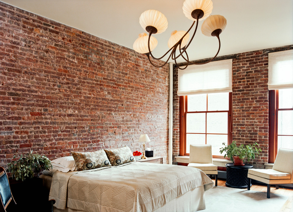 Large industrial master bedroom in New York with light hardwood floors and red walls.