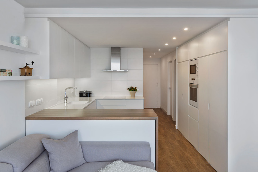 Design ideas for a mid-sized scandinavian u-shaped open plan kitchen in Alicante-Costa Blanca with an undermount sink, flat-panel cabinets, white cabinets, quartz benchtops, white splashback, ceramic splashback, white appliances, porcelain floors, a peninsula, brown floor and white benchtop.