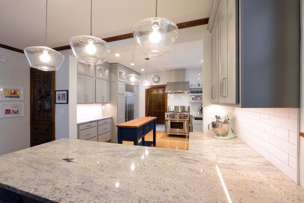 Example of a mid-sized transitional light wood floor and brown floor enclosed kitchen design with a farmhouse sink, shaker cabinets, gray cabinets, wood countertops, white backsplash, porcelain backsplash, stainless steel appliances, an island and brown countertops
