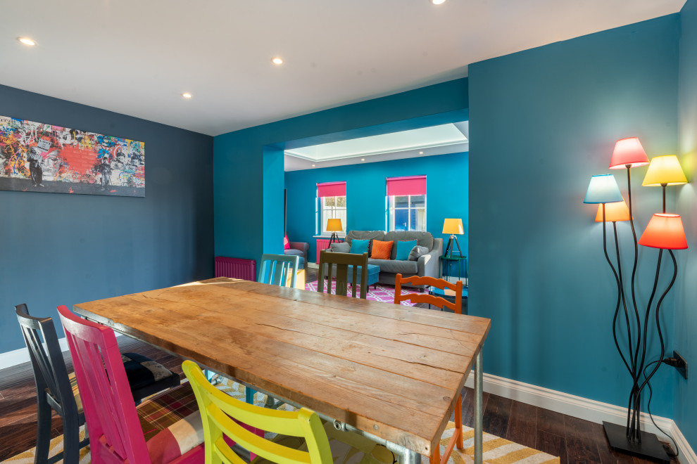 Cette image montre une salle à manger ouverte sur le salon design de taille moyenne avec un mur bleu, parquet foncé, un sol marron et éclairage.