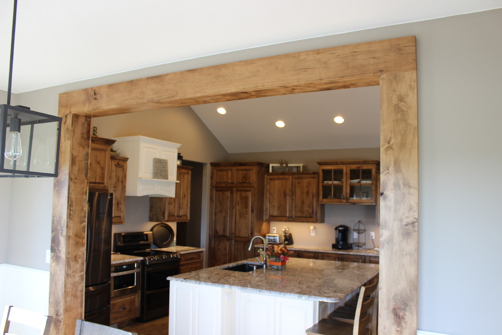Open concept kitchen - large rustic l-shaped medium tone wood floor and brown floor open concept kitchen idea with an undermount sink, raised-panel cabinets, medium tone wood cabinets, granite countertops, stainless steel appliances and an island