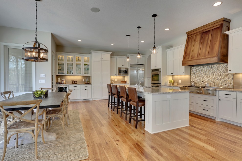 Inspiration for a large transitional l-shaped eat-in kitchen in Minneapolis with an undermount sink, shaker cabinets, white cabinets, beige splashback, mosaic tile splashback, stainless steel appliances, light hardwood floors and with island.