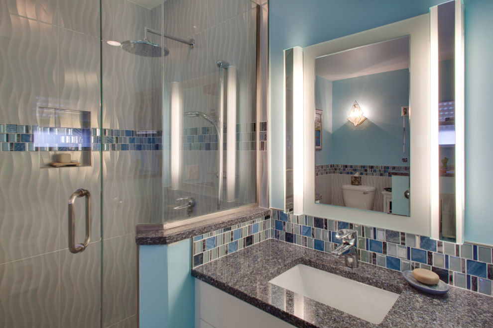 This is an example of a mid-sized beach style 3/4 bathroom in Tampa with flat-panel cabinets, white cabinets, a japanese tub, a corner shower, a two-piece toilet, multi-coloured tile, mosaic tile, blue walls, marble floors, an undermount sink, granite benchtops, grey floor and a hinged shower door.