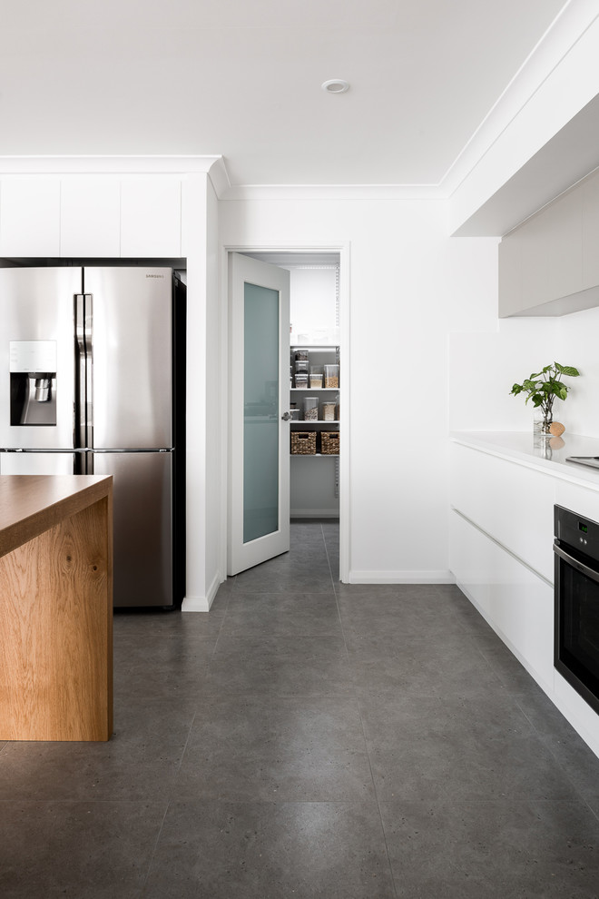 This is an example of a large modern galley open plan kitchen in Perth with a drop-in sink, flat-panel cabinets, white cabinets, quartz benchtops, white splashback, porcelain splashback, stainless steel appliances, porcelain floors, with island and brown floor.