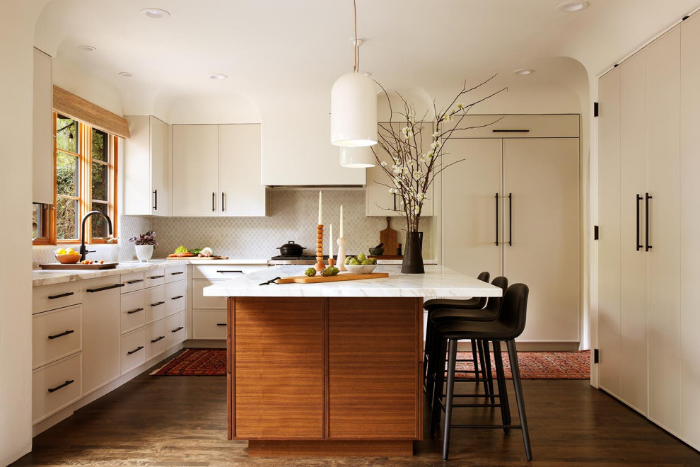 Photo of a mid-sized u-shaped eat-in kitchen in San Francisco with flat-panel cabinets, white cabinets, marble benchtops, white splashback, with island, white benchtop, dark hardwood floors and brown floor.