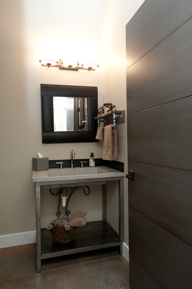 This is an example of a large industrial powder room in Other with a one-piece toilet, gray tile, grey walls, concrete floors and an integrated sink.