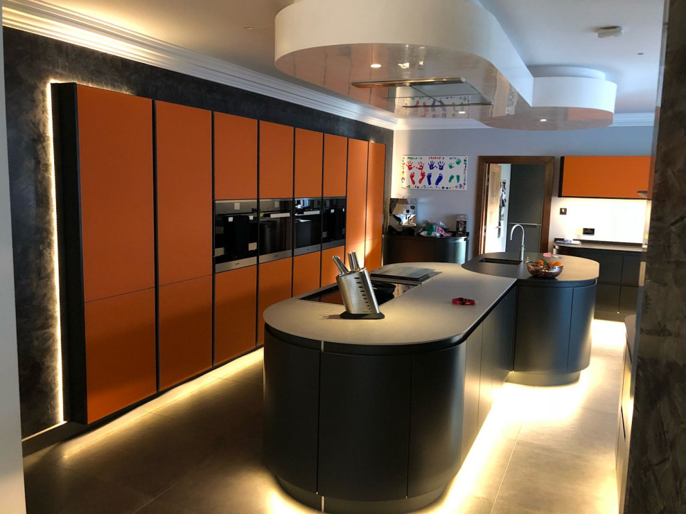 This is an example of a large contemporary l-shaped open plan kitchen in Other with a drop-in sink, flat-panel cabinets, orange cabinets, quartz benchtops, grey splashback, ceramic splashback, stainless steel appliances, ceramic floors, multiple islands, grey floor and grey benchtop.