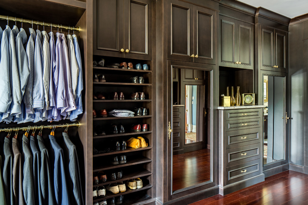 This is an example of a large traditional men's walk-in wardrobe in New York with dark wood cabinets, medium hardwood floors and recessed-panel cabinets.