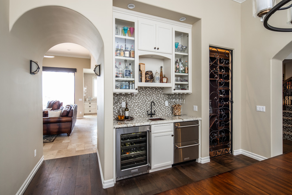 Photo of a mid-sized transitional single-wall wet bar in San Diego with an undermount sink, recessed-panel cabinets, white cabinets, granite benchtops, multi-coloured splashback, mosaic tile splashback, dark hardwood floors, brown floor and multi-coloured benchtop.