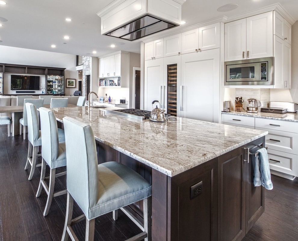 Design ideas for a large transitional galley open plan kitchen in Seattle with an undermount sink, recessed-panel cabinets, white cabinets, panelled appliances, dark hardwood floors, with island, brown floor, beige benchtop, granite benchtops, brown splashback and stone tile splashback.