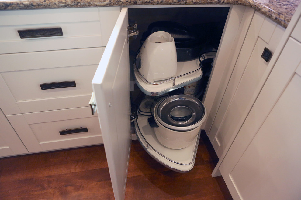 Example of a mid-sized transitional l-shaped medium tone wood floor and brown floor open concept kitchen design in Calgary with an undermount sink, shaker cabinets, white cabinets, granite countertops, white backsplash, mosaic tile backsplash, stainless steel appliances, an island and beige countertops