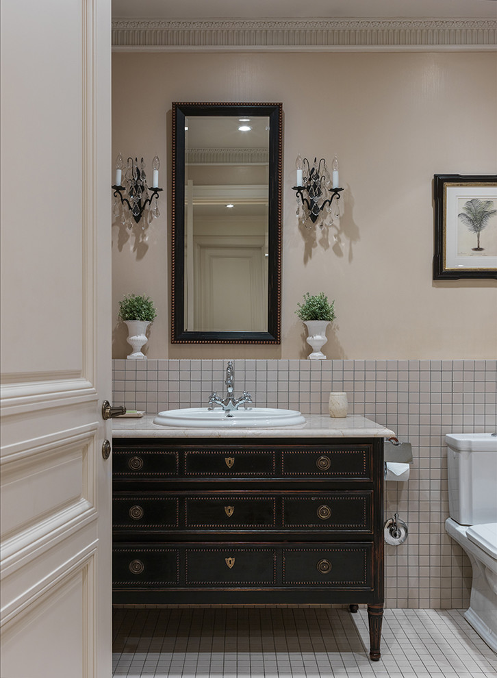 This is an example of a mid-sized traditional master bathroom in Other with black cabinets, an alcove tub, beige tile, ceramic tile, beige walls, ceramic floors, a drop-in sink, marble benchtops, beige floor, a two-piece toilet and flat-panel cabinets.