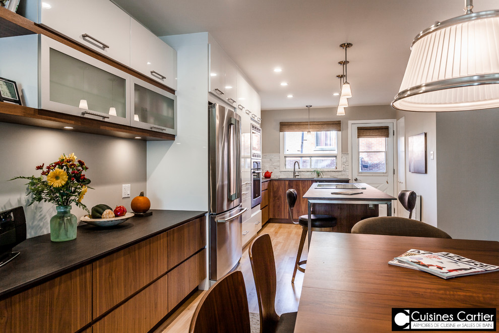 Example of a large transitional galley medium tone wood floor eat-in kitchen design in Montreal with an undermount sink, flat-panel cabinets, dark wood cabinets, quartzite countertops, white backsplash, mosaic tile backsplash, stainless steel appliances and an island