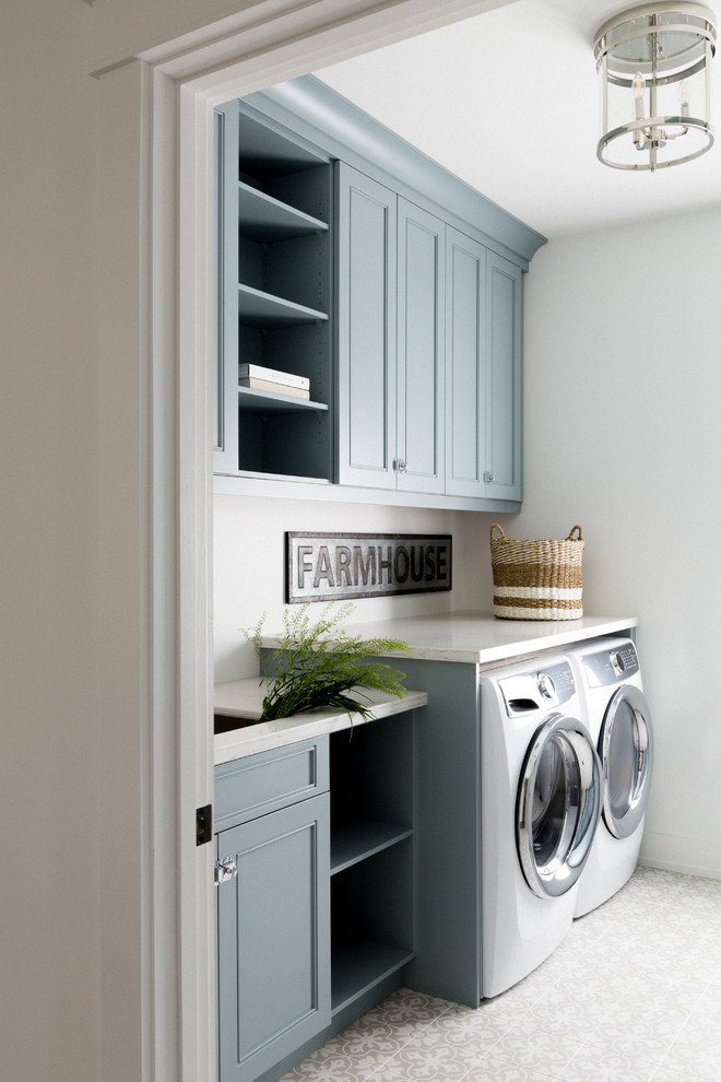 Photo of a mid-sized transitional galley dedicated laundry room in Toronto with an undermount sink, beaded inset cabinets, blue cabinets, quartz benchtops, white walls, porcelain floors, a side-by-side washer and dryer, white floor and white benchtop.