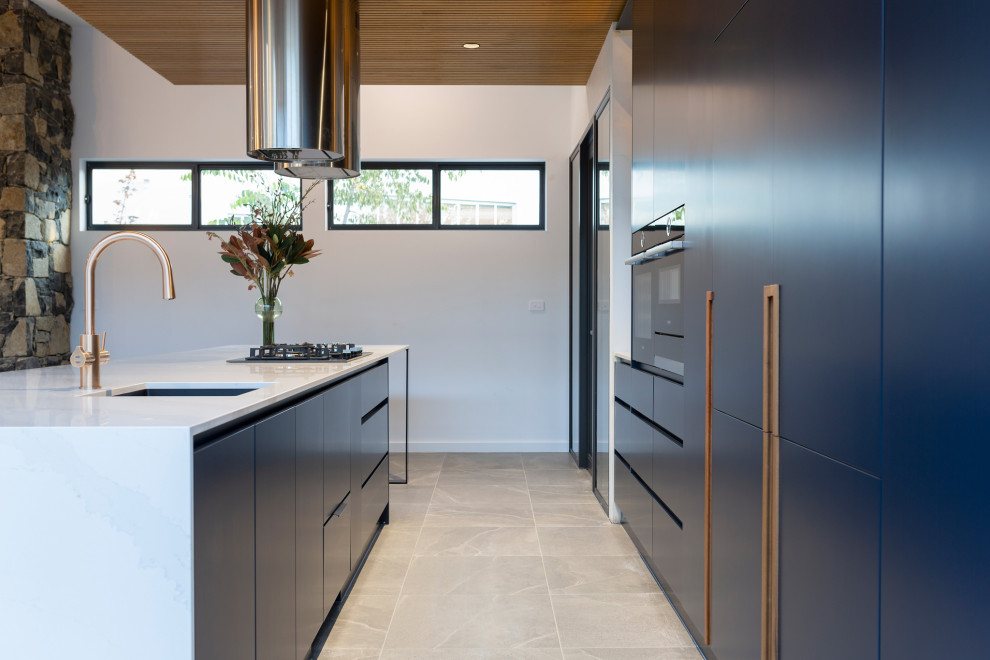 Large modern galley open plan kitchen in Canberra - Queanbeyan with an undermount sink, blue cabinets, quartz benchtops, black appliances, porcelain floors, with island, grey floor and white benchtop.