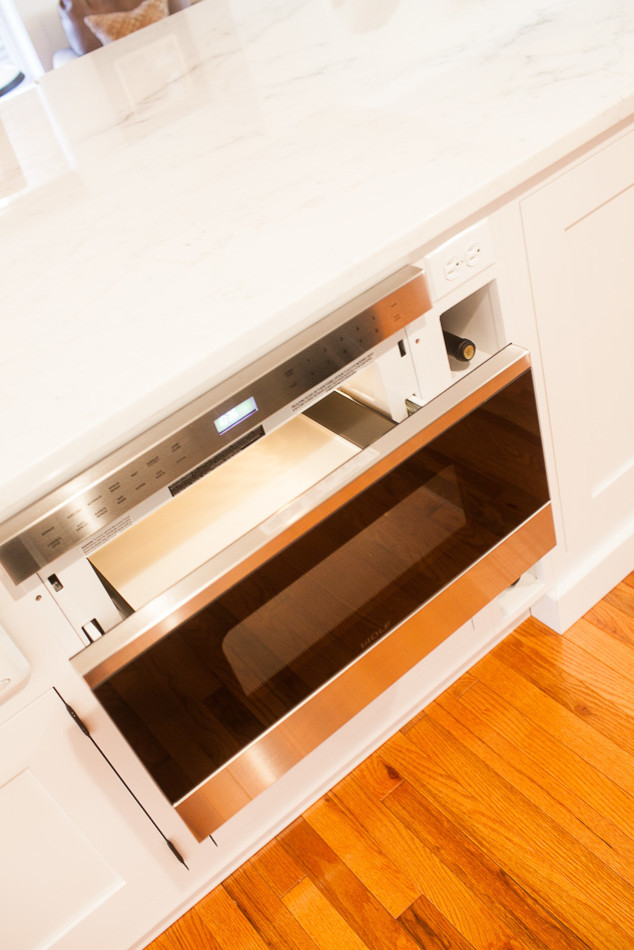 Eat-in kitchen - large transitional medium tone wood floor eat-in kitchen idea in St Louis with a farmhouse sink, flat-panel cabinets, white cabinets, white backsplash, subway tile backsplash, stainless steel appliances and an island