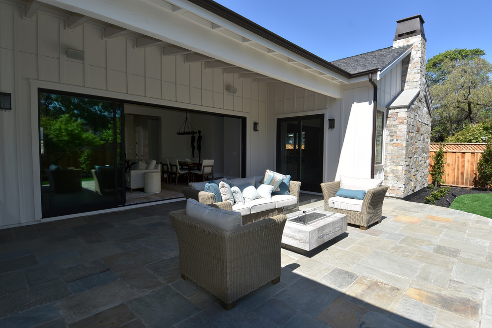 This is an example of a mid-sized country backyard patio in San Francisco with a fire feature, natural stone pavers and a roof extension.