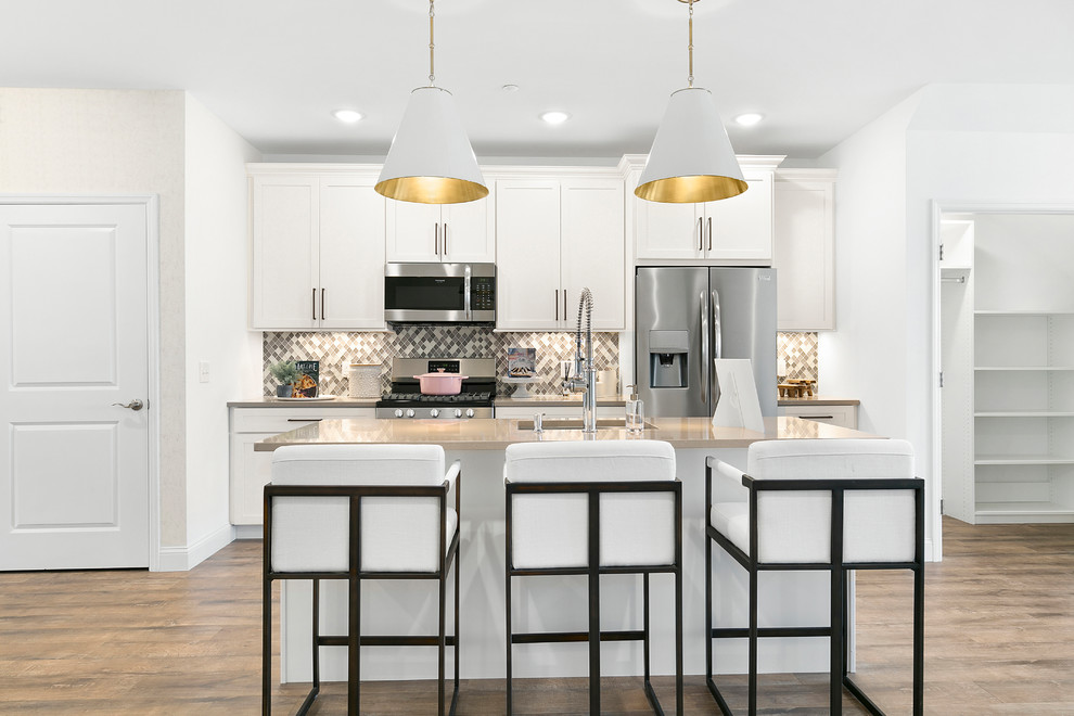 Photo of a mid-sized contemporary single-wall kitchen in New York with medium hardwood floors, brown floor, an undermount sink, shaker cabinets, white cabinets, multi-coloured splashback, stainless steel appliances, beige benchtop and with island.