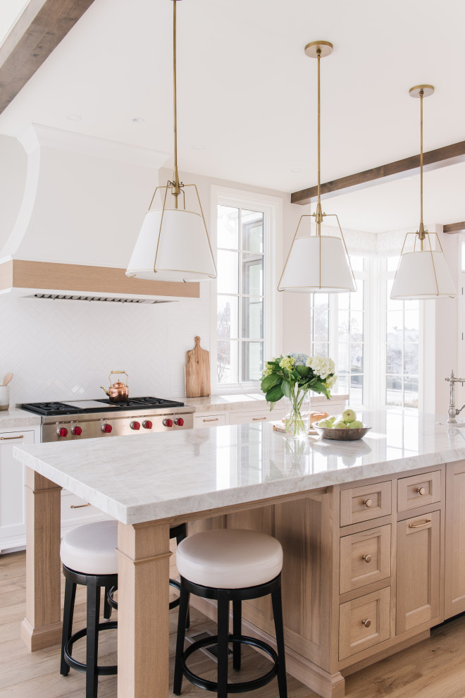 This is an example of a medium sized traditional u-shaped kitchen/diner in Salt Lake City with a belfast sink, shaker cabinets, white cabinets, quartz worktops, white splashback, metro tiled splashback, integrated appliances, light hardwood flooring, an island, white worktops and exposed beams.