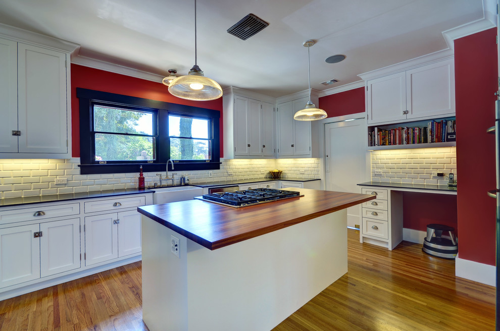 This is an example of a transitional u-shaped separate kitchen in Los Angeles with a farmhouse sink, shaker cabinets, white cabinets, soapstone benchtops, white splashback, subway tile splashback, stainless steel appliances, light hardwood floors and with island.