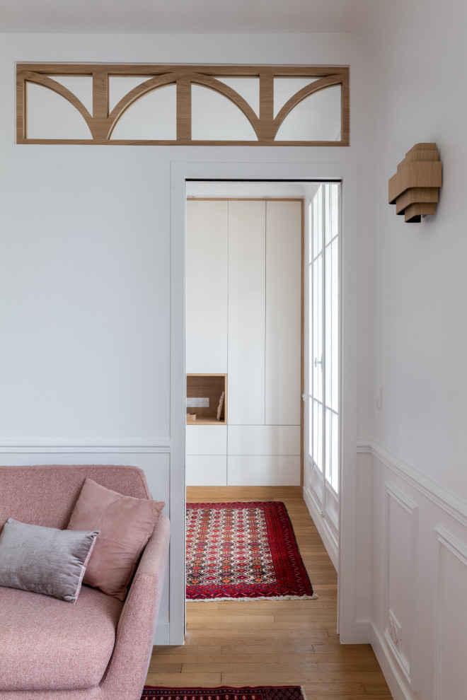 Пример оригинального дизайна: гостиная комната среднего размера, в белых тонах с отделкой деревом в скандинавском стиле с с книжными шкафами и полками, белыми стенами, светлым паркетным полом и панелями на стенах
