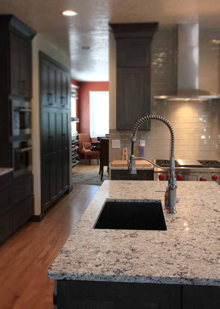 Example of a large transitional u-shaped light wood floor eat-in kitchen design in Cedar Rapids with an undermount sink, shaker cabinets, dark wood cabinets, granite countertops, gray backsplash, glass tile backsplash, stainless steel appliances and an island