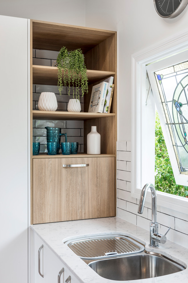 Mid-sized contemporary l-shaped open plan kitchen in Brisbane with an undermount sink, flat-panel cabinets, white cabinets, quartz benchtops, white splashback, ceramic splashback, white appliances, medium hardwood floors, with island and brown floor.