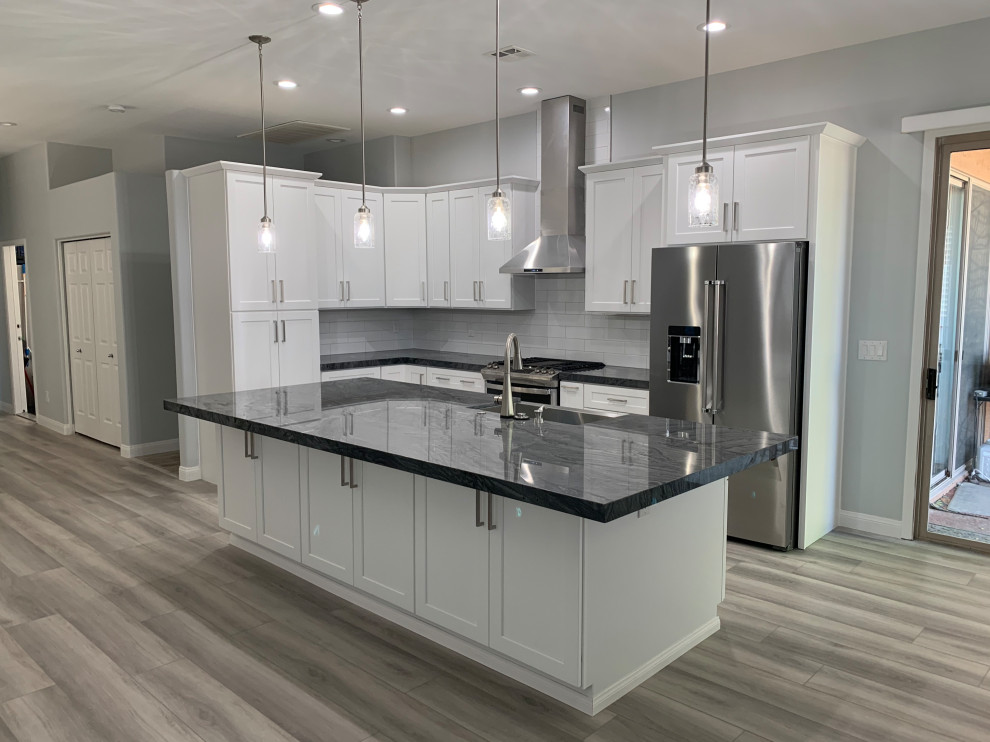 Design ideas for a mid-sized modern eat-in kitchen in Las Vegas with a farmhouse sink, shaker cabinets, white cabinets, quartzite benchtops, white splashback, cement tile splashback, stainless steel appliances, laminate floors, with island, grey floor and grey benchtop.