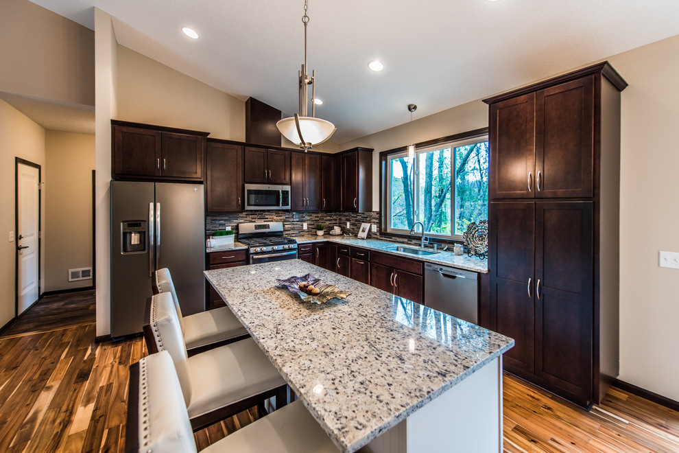 Eat-in kitchen - mid-sized transitional l-shaped brown floor and medium tone wood floor eat-in kitchen idea in Minneapolis with an undermount sink, shaker cabinets, dark wood cabinets, granite countertops, multicolored backsplash, matchstick tile backsplash, stainless steel appliances and an island