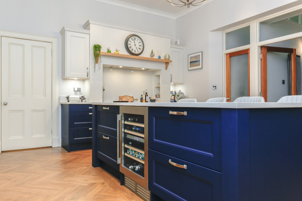 This is an example of a medium sized traditional l-shaped kitchen/diner in Glasgow with shaker cabinets, blue cabinets, white splashback, an island, white worktops, a single-bowl sink, black appliances and feature lighting.