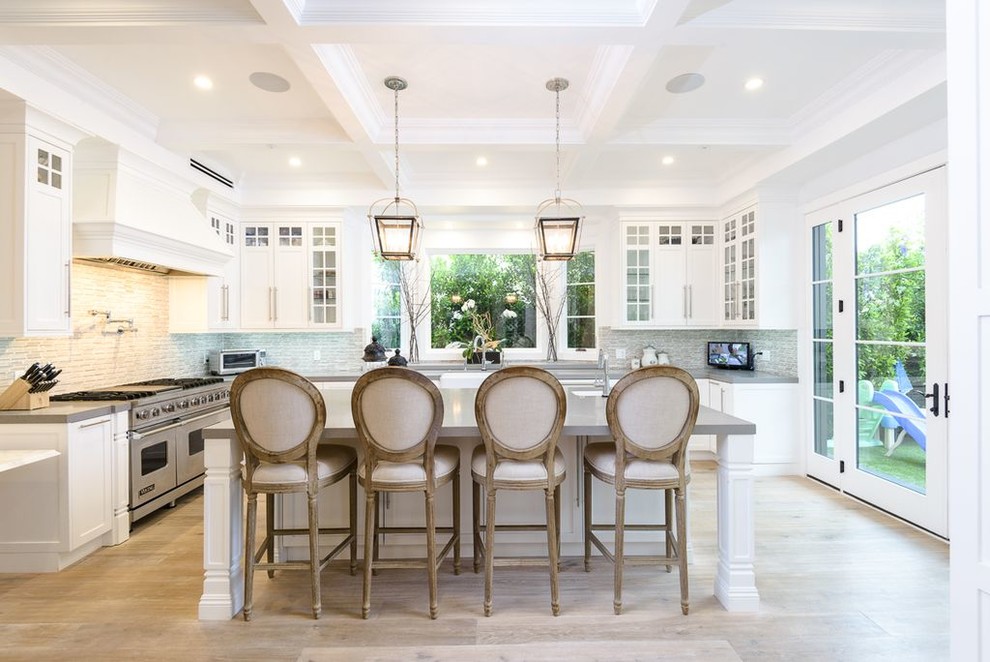 Design ideas for a large transitional u-shaped open plan kitchen in Los Angeles with glass-front cabinets, white cabinets, grey splashback, stainless steel appliances, light hardwood floors, with island, grey benchtop, a farmhouse sink, solid surface benchtops and beige floor.