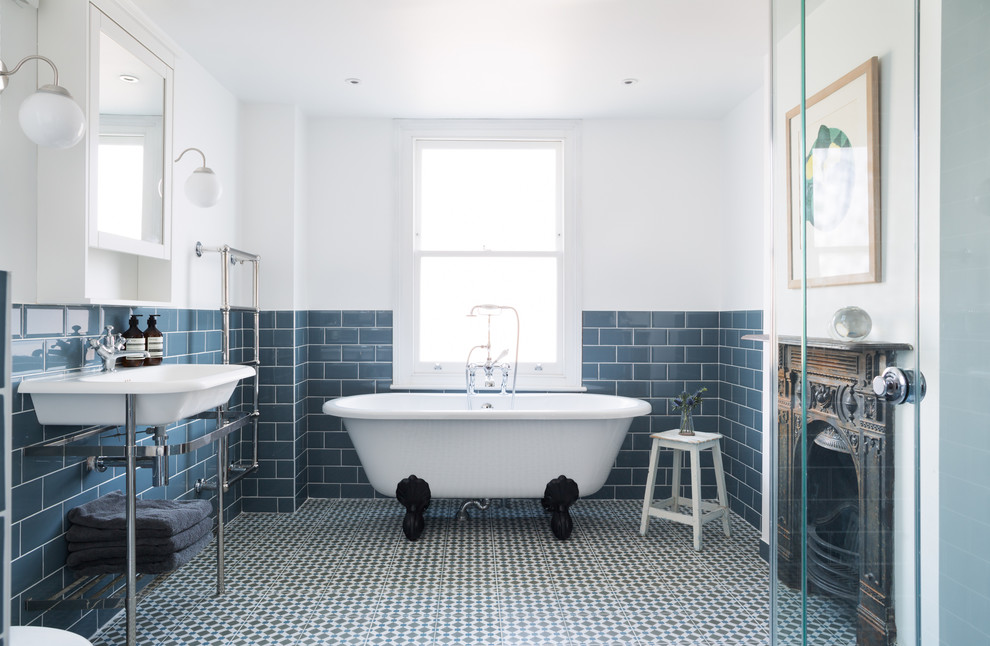 Photo of a transitional master bathroom in London with open cabinets, a claw-foot tub, blue tile, subway tile, white walls and a console sink.