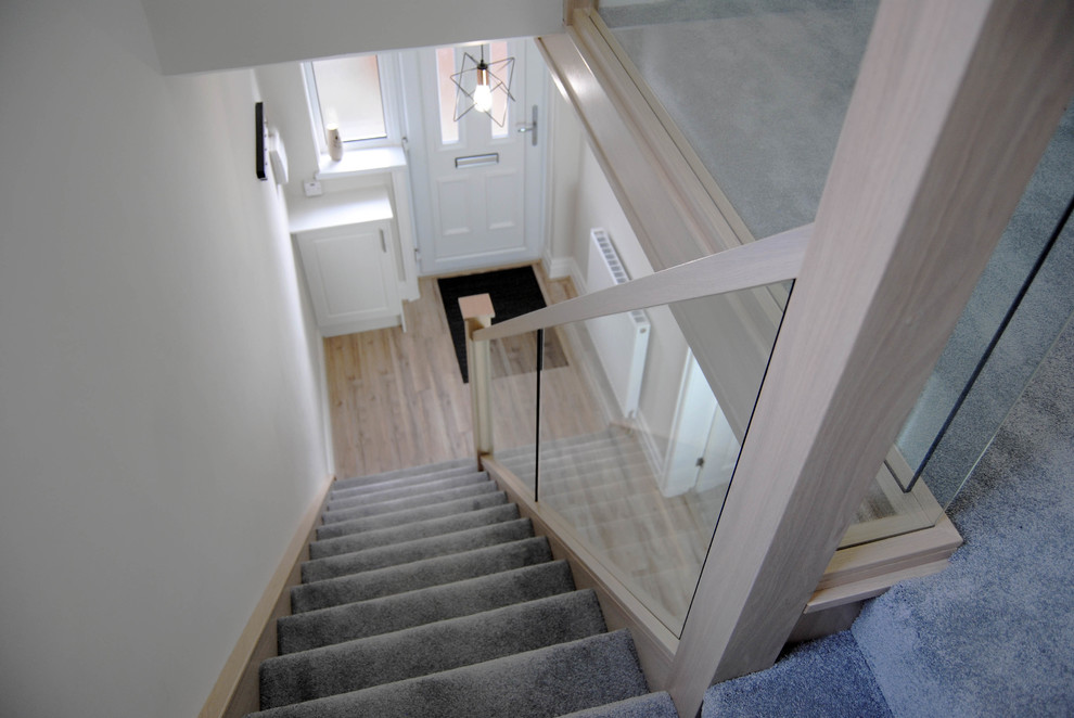 Photo of a small contemporary carpeted straight staircase in Manchester with carpet risers and glass railing.