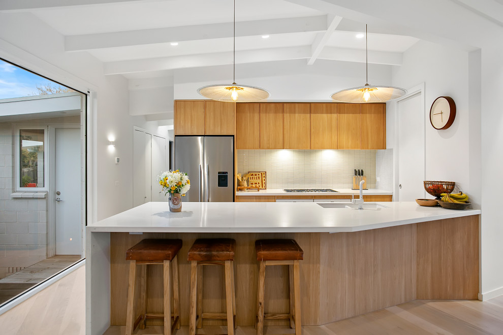 Beach style open plan kitchen in Melbourne with a submerged sink, light wood cabinets, engineered stone countertops, white appliances, light hardwood flooring, an island and white worktops.