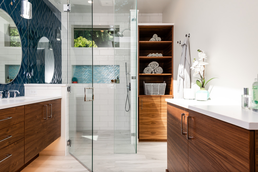 This is an example of a mid-sized modern master bathroom in Seattle with flat-panel cabinets, brown cabinets, a curbless shower, a two-piece toilet, blue tile, porcelain tile, white walls, porcelain floors, an undermount sink, engineered quartz benchtops, grey floor, a hinged shower door, white benchtops, a niche, a double vanity, a built-in vanity and decorative wall panelling.