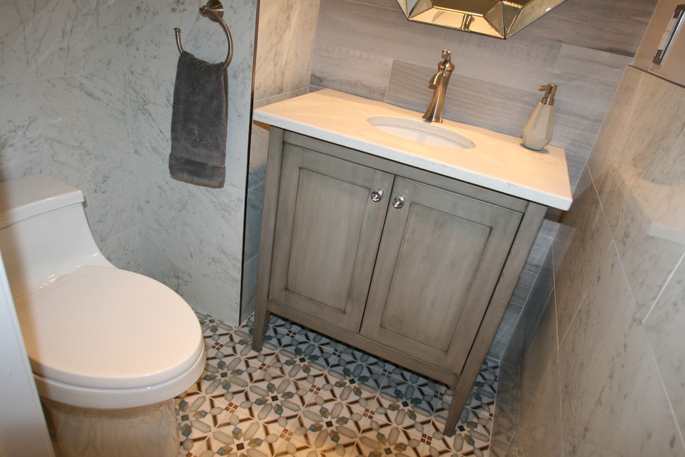 Photo of a small mediterranean powder room in New York with grey cabinets, a one-piece toilet, white tile, porcelain tile, white walls, cement tiles, an undermount sink, engineered quartz benchtops, multi-coloured floor, furniture-like cabinets, white benchtops, a freestanding vanity and vaulted.