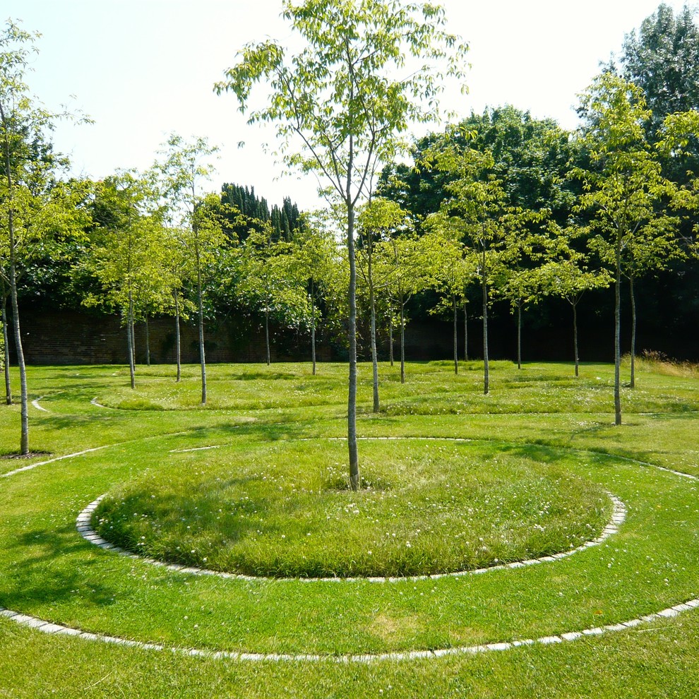 Expansive country backyard full sun formal garden in Oxfordshire with a garden path and river rock for spring.