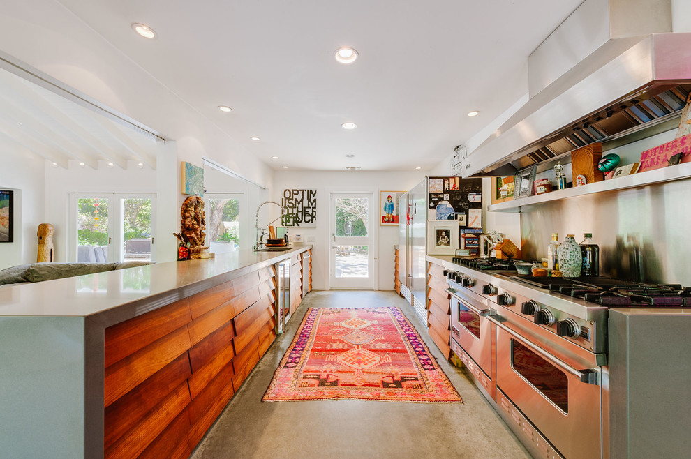 Inspiration for a mid-sized eclectic galley open plan kitchen in Los Angeles with stainless steel appliances, concrete floors, a double-bowl sink, louvered cabinets, medium wood cabinets and solid surface benchtops.