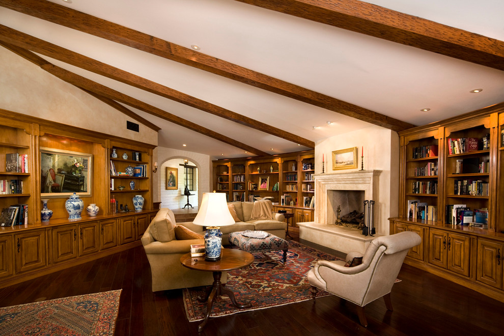 Photo of a large mediterranean enclosed living room in Santa Barbara with a library, a standard fireplace, white walls, dark hardwood floors and a stone fireplace surround.