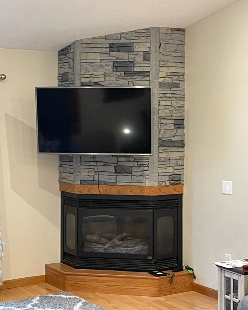 На фото: гостиная комната с угловым камином, фасадом камина из каменной кладки и телевизором на стене с