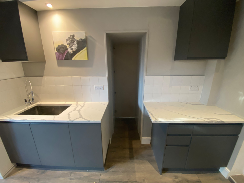 This is an example of a large contemporary galley utility room in London with a built-in sink, flat-panel cabinets, grey cabinets, quartz worktops, white splashback, porcelain splashback, beige walls, laminate floors, a side by side washer and dryer, grey floors and multicoloured worktops.
