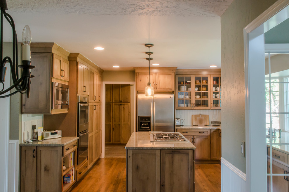 Mid-sized mountain style u-shaped medium tone wood floor enclosed kitchen photo with a farmhouse sink, shaker cabinets, medium tone wood cabinets, granite countertops, beige backsplash, ceramic backsplash, stainless steel appliances and an island