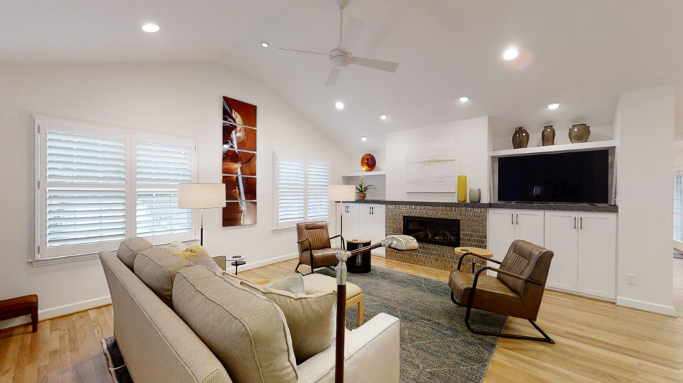 Cette image montre une grande salle de séjour design ouverte avec un mur blanc, parquet clair, une cheminée standard, un manteau de cheminée en carrelage, un téléviseur encastré, un sol marron et un plafond voûté.