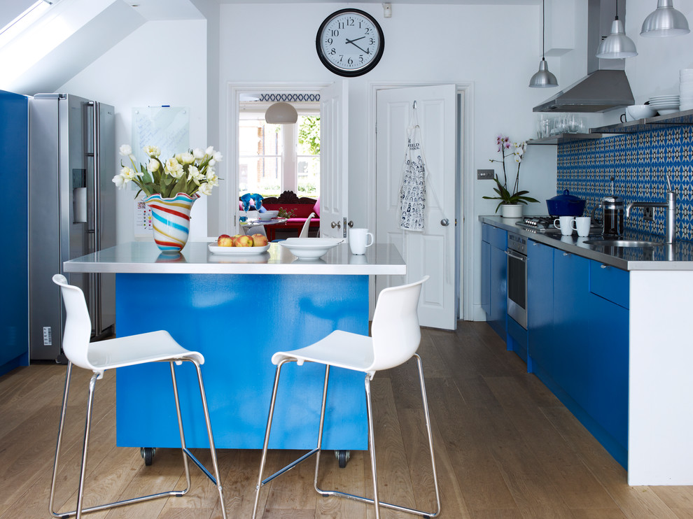 Contemporary galley separate kitchen in London with a single-bowl sink, flat-panel cabinets, blue cabinets, multi-coloured splashback, stainless steel appliances, medium hardwood floors and with island.