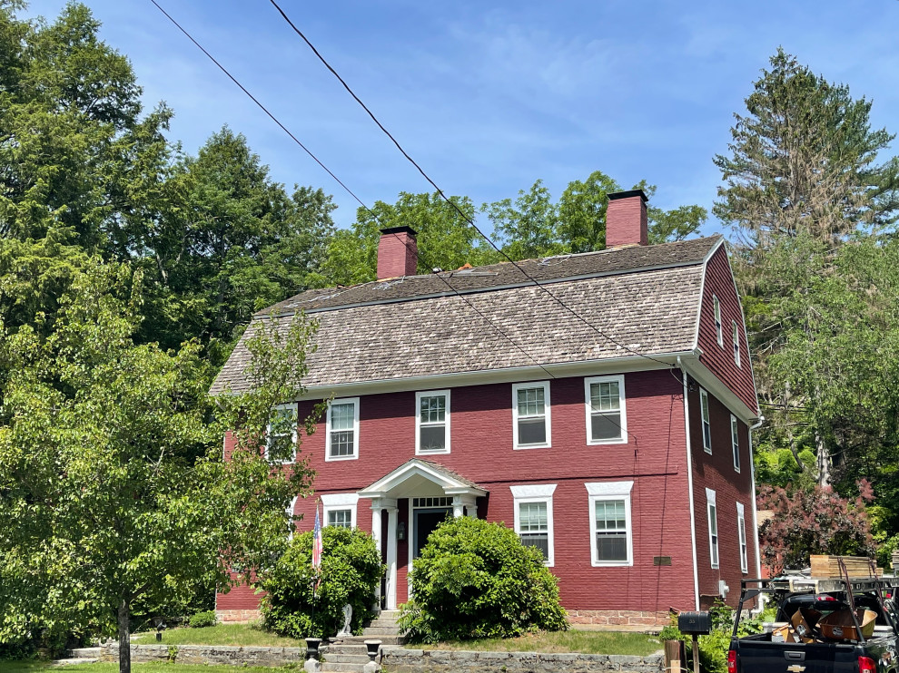 Photo of a large traditional three-storey red house exterior in Bridgeport with painted brick siding, a gambrel roof, a shingle roof and a red roof.
