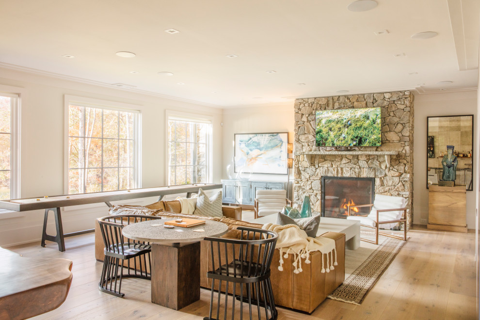 Photo of a large beach style open concept family room in Other with a game room, white walls, light hardwood floors, a standard fireplace, a stone fireplace surround, a wall-mounted tv and brown floor.