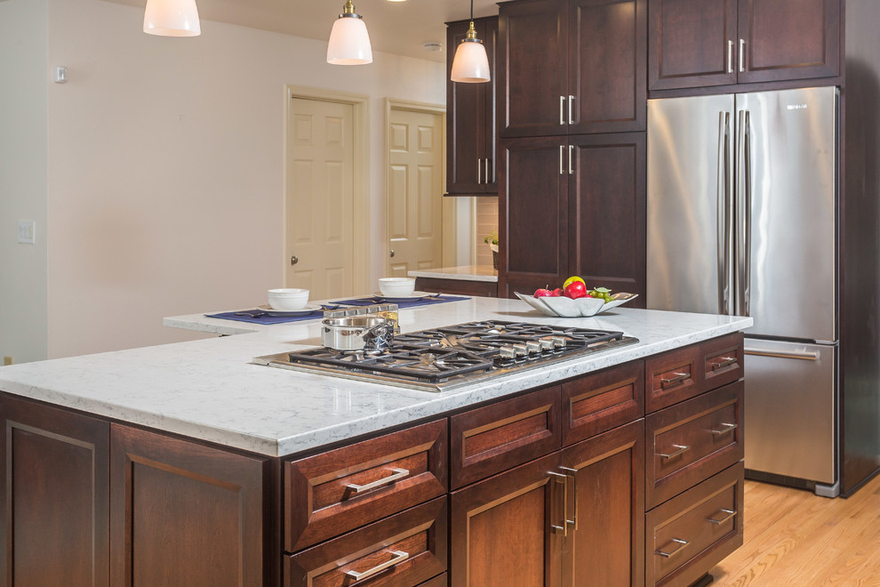 Open concept kitchen - mid-sized transitional l-shaped light wood floor open concept kitchen idea with an undermount sink, recessed-panel cabinets, dark wood cabinets, quartz countertops, gray backsplash, subway tile backsplash, stainless steel appliances and an island