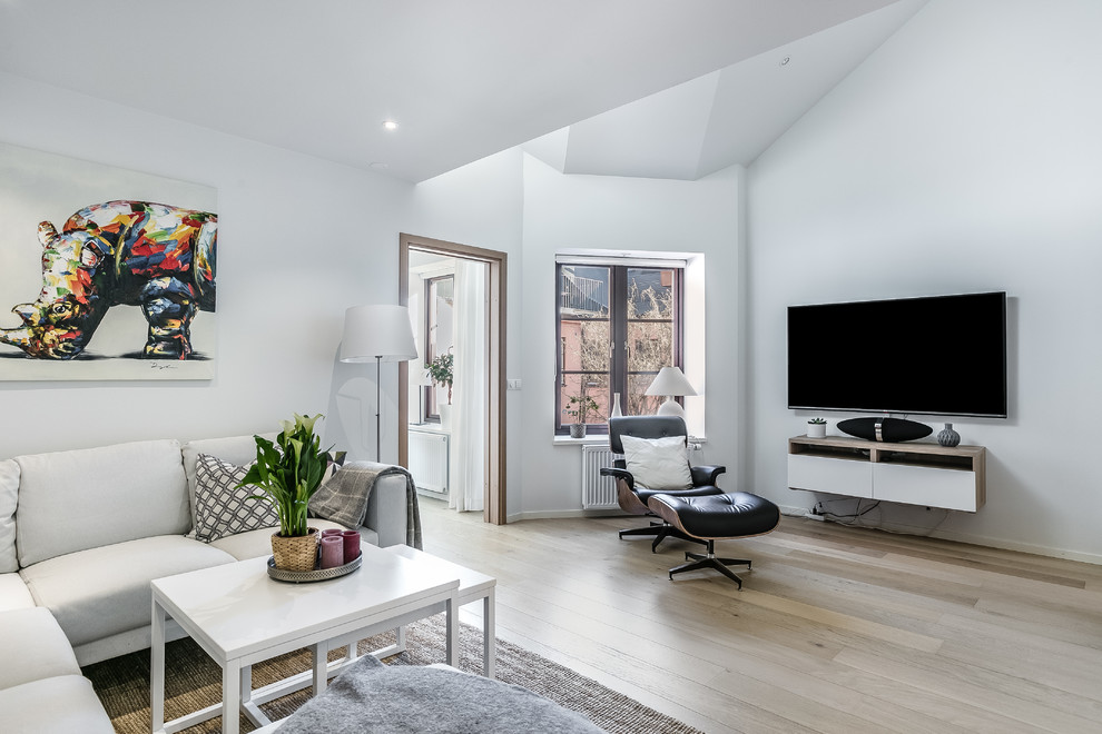 This is an example of a scandinavian living room in Malmo with white walls, light hardwood floors, a wall-mounted tv and beige floor.