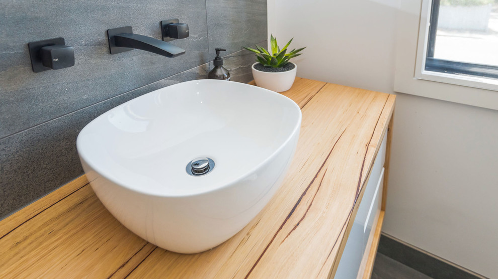 This is an example of a contemporary bathroom in Melbourne with white cabinets, gray tile, stone tile, white walls, a vessel sink and wood benchtops.